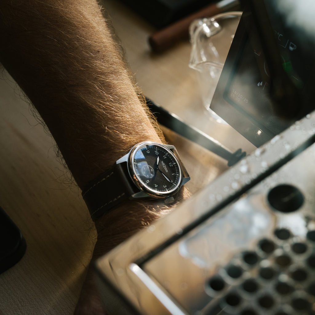 Close-up of a person's wrist wearing a black wristwatch with a blurred background